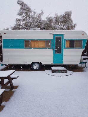 Experience the charm of a vintage camper van, complete with a turquoise stripe and blue door, surrounded by serene winter landscapes.