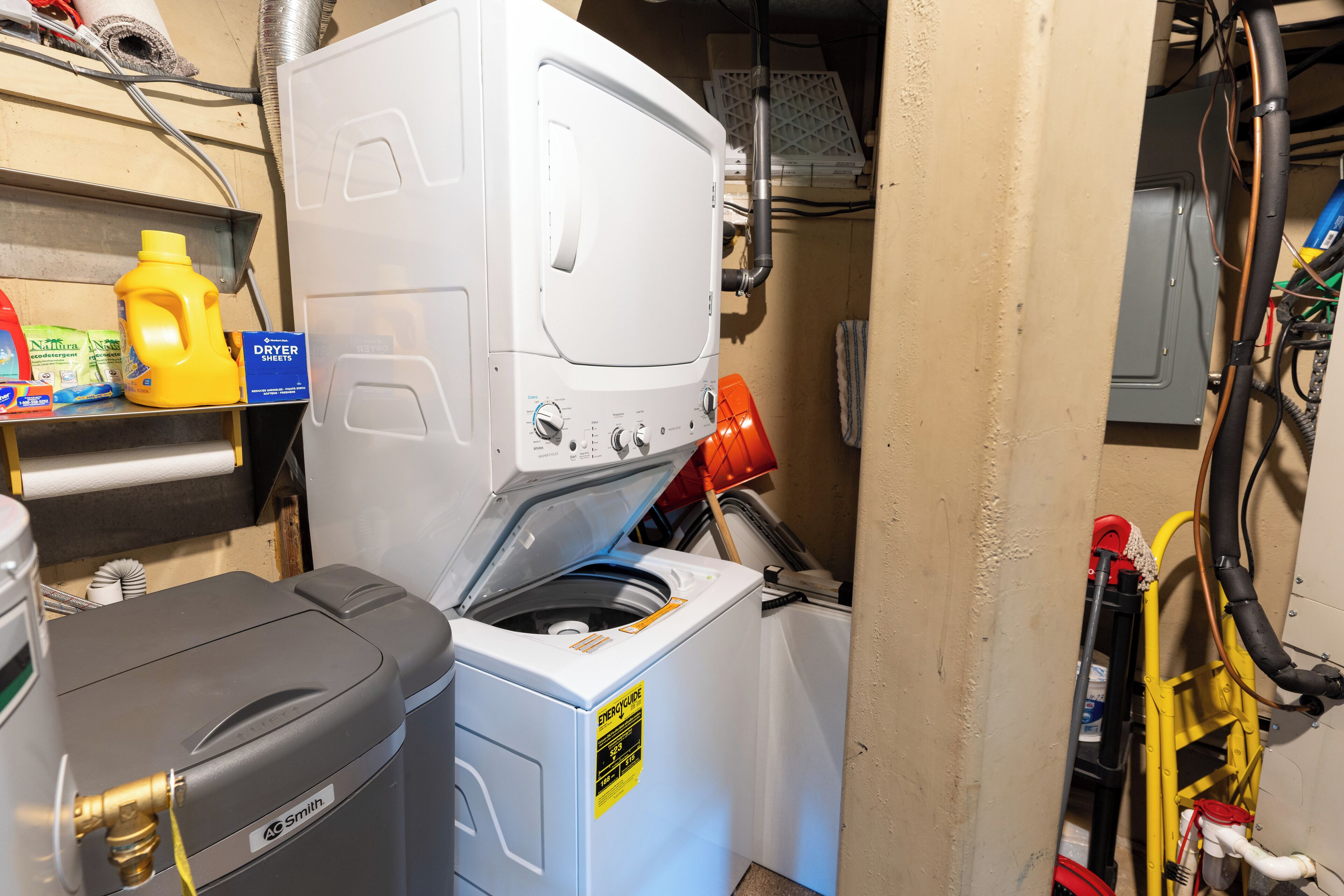A compact laundry room with a front-loading washer and dryer, a utility cart, and various cleaning supplies on a shelf.