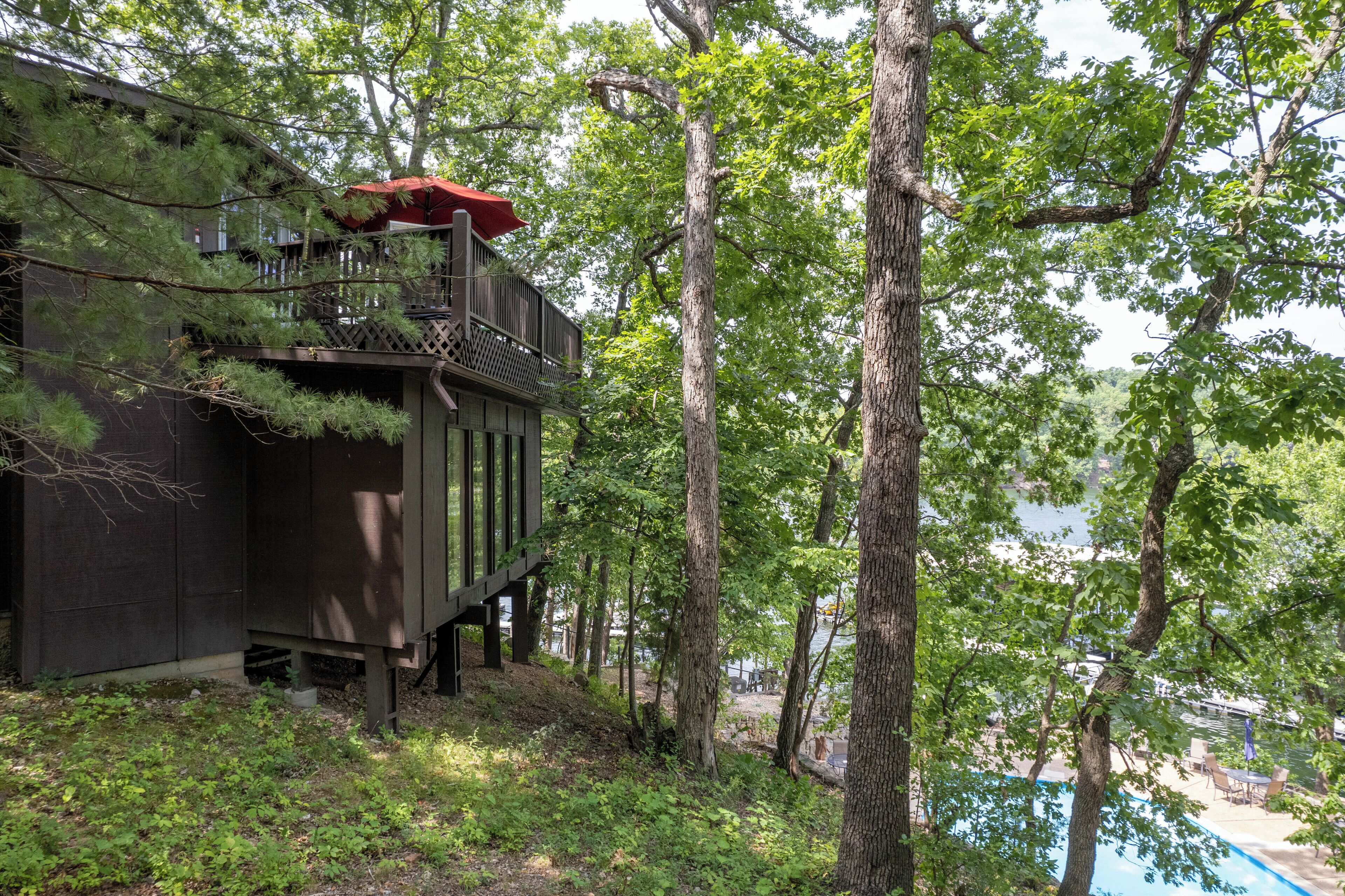 A wooden cabin with a balcony, surrounded by trees and a swimming pool.