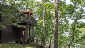 A wooden cabin with a balcony, surrounded by trees and a swimming pool.