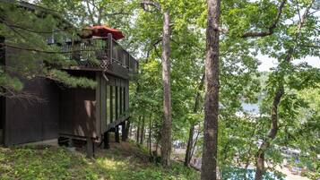 A wooden cabin with a balcony, surrounded by trees and a swimming pool.