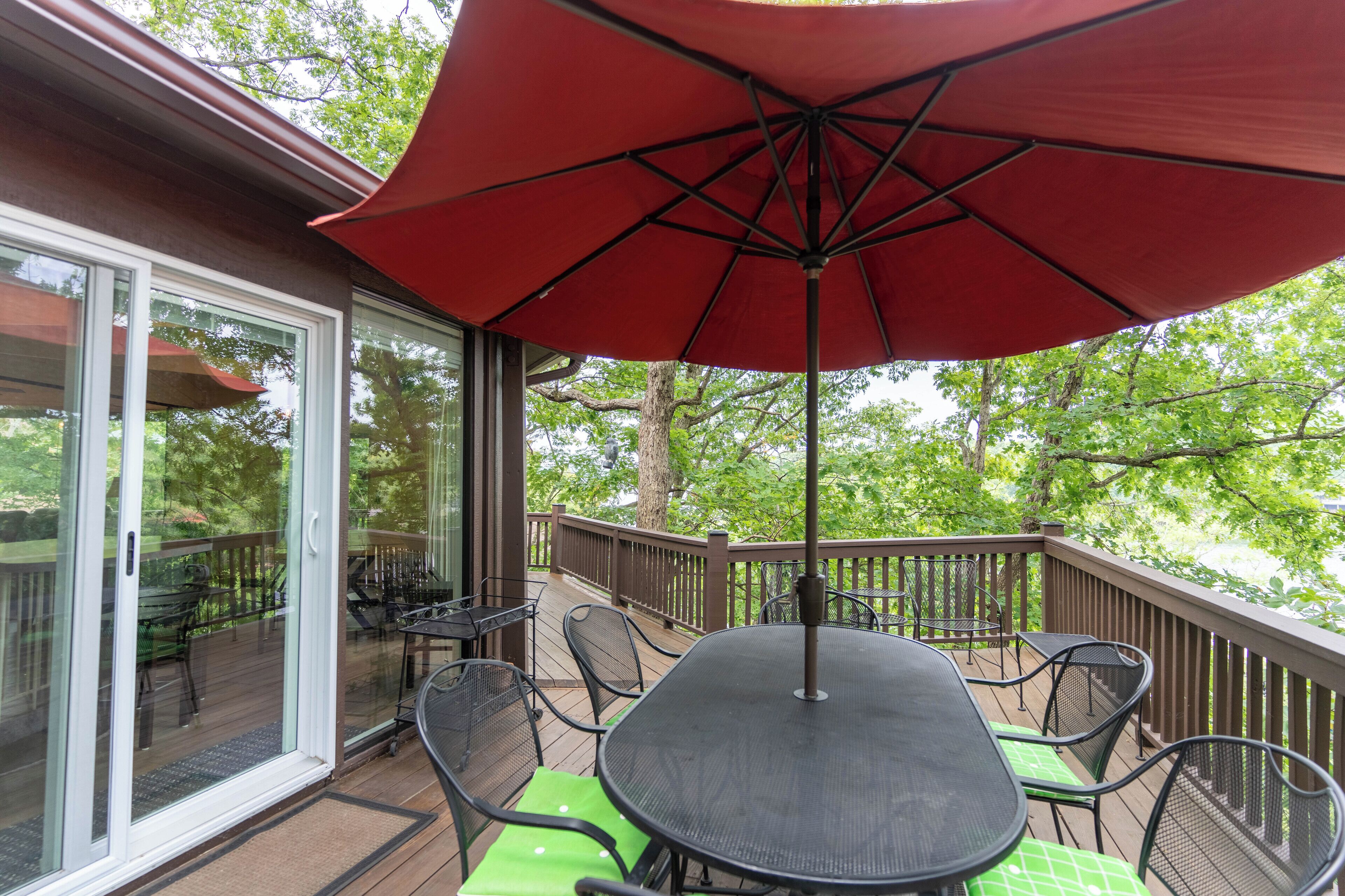 A covered outdoor deck with a table and chairs, a red umbrella, and a glass door leading to a patio area.