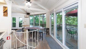 A covered outdoor area with a dining table and chairs, a staircase with a railing, and large sliding glass doors leading to a deck.