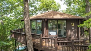 A treehouse with a wooden deck and glass walls, surrounded by trees.