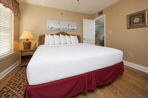A neatly made bed with a white quilt, a red skirt, and a headboard with multiple pillows.