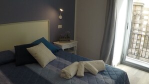Una cama bien hecha con colcha azul, almohadas y toallas dobladas.