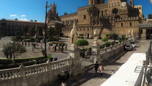 Un edificio histórico con una gran cúpula y múltiples torres, rodeado de una plaza bien cuidada con estatuas y una fuente.