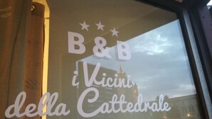 Una ventana con el texto "B&B i Vicini della Cattedrale" y el reflejo de un edificio.