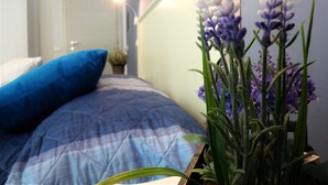 Un dormitorio con una cama, una almohada azul y una planta en maceta con flores moradas.
