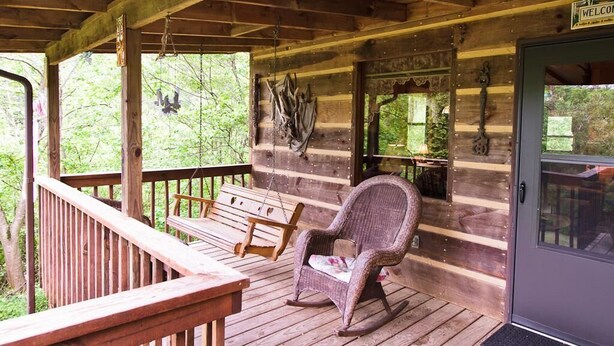 A wooden porch with a rocking chair and a bench, a door with a 'Welcome' sign, and a view of greenery.