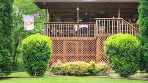 A wooden cabin with a balcony, surrounded by well-maintained bushes and trees.