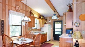 A cozy cabin-style kitchen with wooden walls, a dining table with wicker chairs, a refrigerator, and a small island with a lamp.