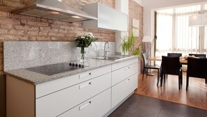 Une cuisine moderne dotée de plans de travail en granit, de meubles blancs, d’une hotte en acier inoxydable et d’un coin repas avec une table et des chaises en bois.