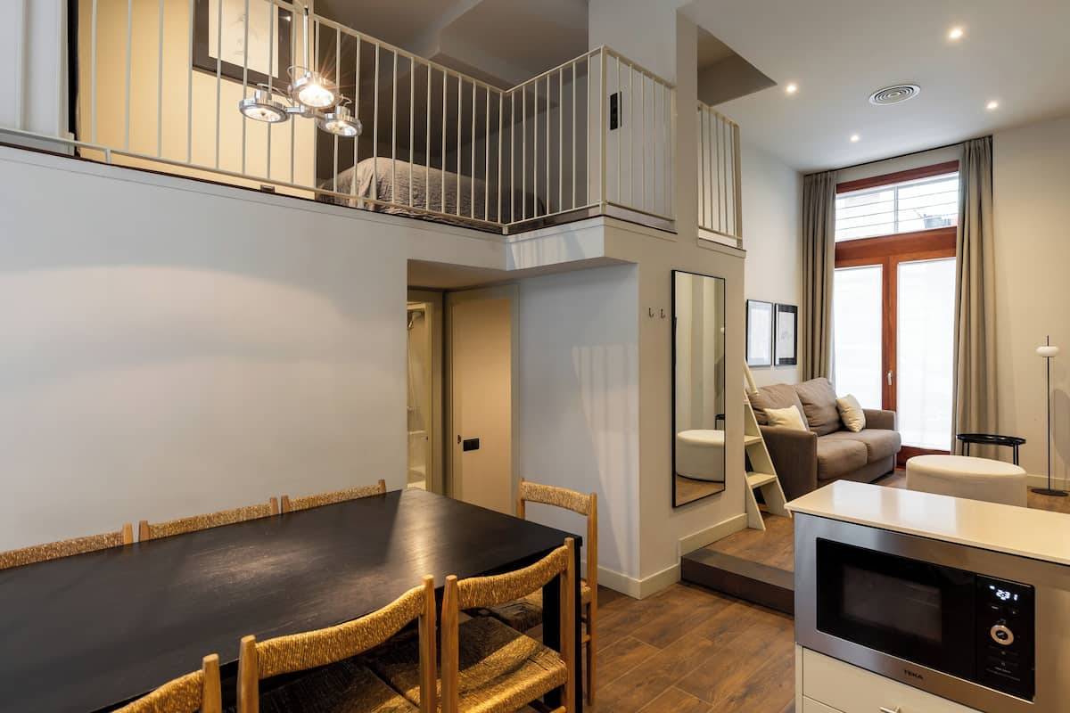 A modern apartment with a dining area, kitchenette, and a loft bedroom with a balcony.