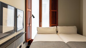 A bedroom with a bed, a TV, and a window with wooden shutters. - Uma Suites Barceloneta Beach (Barcelona)