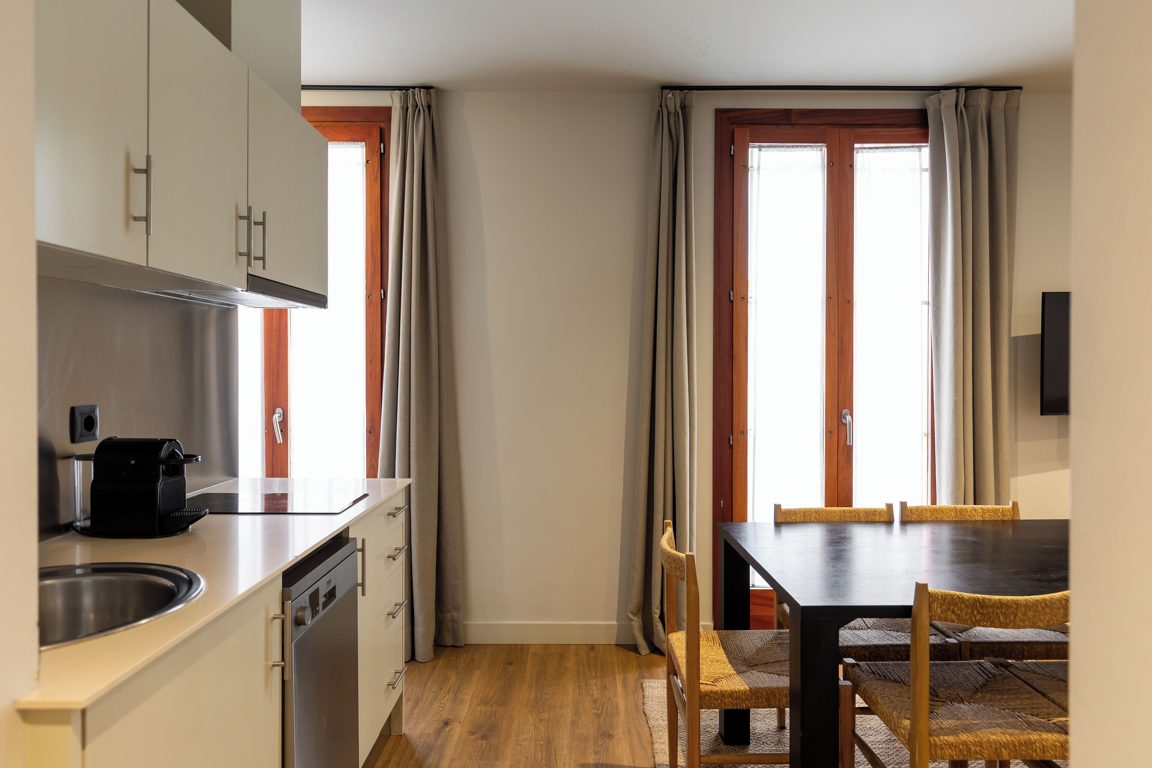 Una cocina funcional con lavabo, lavavajillas y tostadora. Hay una zona de comedor con mesa y sillas.