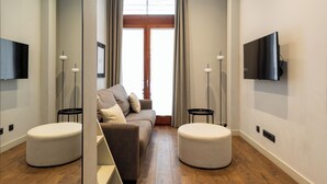A modern living room with a sofa, ottoman, and TV mounted on the wall. - Uma Suites Barceloneta Beach (Barcelona)