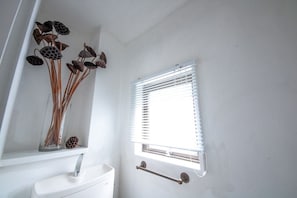 A bathroom with a white sink, a window with blinds, and a decorative vase with dried flowers.