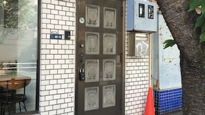 Un edificio con fachada de ladrillo, una puerta grande en arco con paneles de vidrio decorativos y una ventana visible con una mesa y sillas afuera.