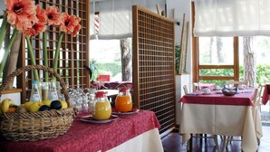 A dining area with tables set for breakfast, featuring fruit baskets, juice pitchers, and a decorative screen with flowers. - Hotel Friuli (Lignano Sabbiadoro)
