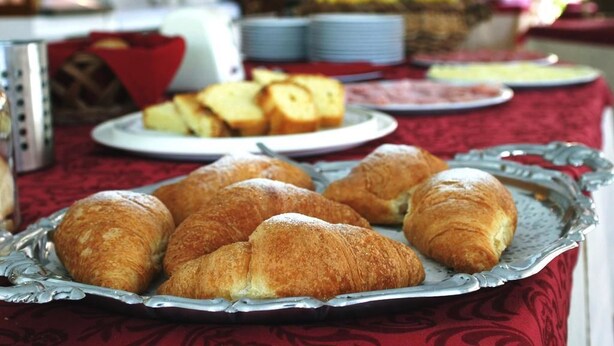 A breakfast buffet with croissants and bread on a table covered with a red tablecloth. - Hotel Friuli (Lignano Sabbiadoro)