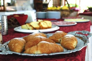 A breakfast buffet with croissants and bread on a table covered with a red tablecloth.