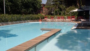 A clear swimming pool with a wooden deck and red and white lounge chairs. - Hotel Friuli (Lignano Sabbiadoro)