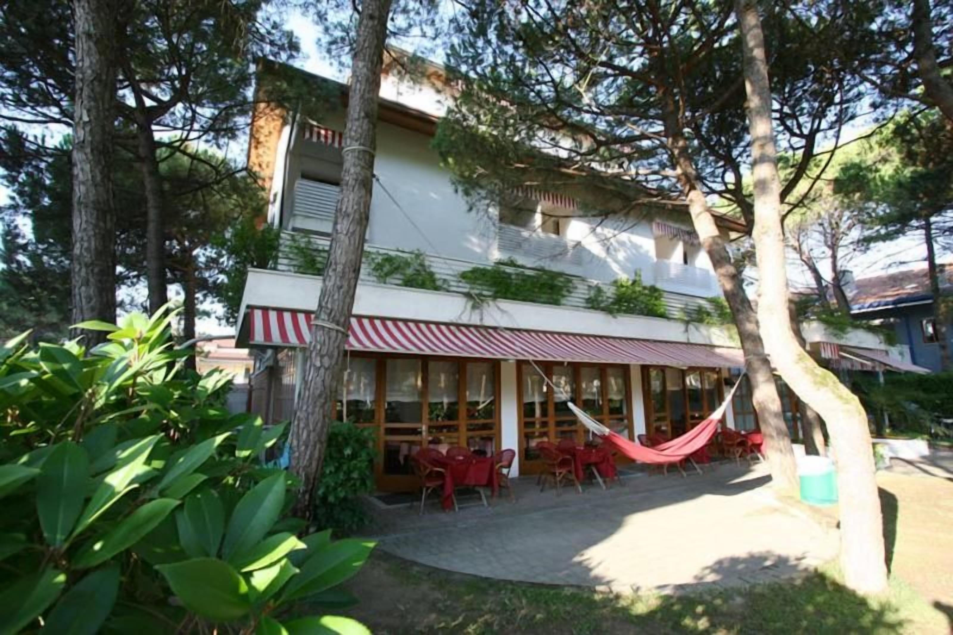 Un edificio con toldo a rayas rojas y blancas, mesas al aire libre con sillas rojas y una hamaca.