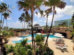 Un resort con area piscina, palme e un edificio dal tetto rosso.