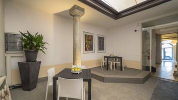 A modern interior with a dining area featuring a black table and white chairs, a potted plant, and a column.