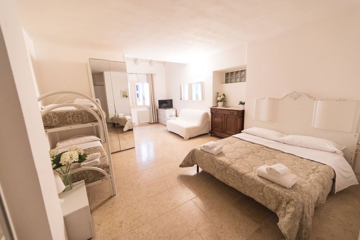 A hotel room with a bed, a chair, a desk, a mirror, and a wardrobe.