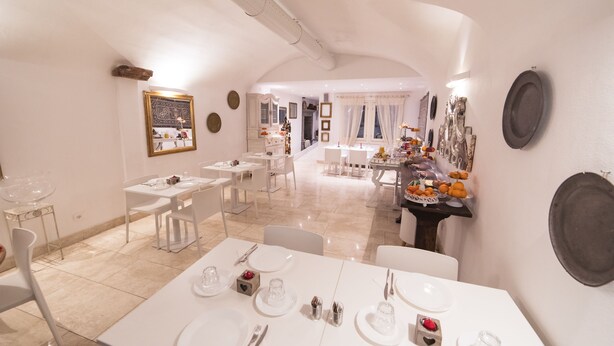 A dining area with white tables and chairs, a buffet table with fruits and dishes, and a mirror on the wall. - Academia Resort (Bergamo)