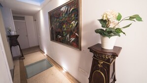 A hallway with a skylight, a large abstract painting, a potted plant, and a wooden cabinet. - Academia Resort (Bergamo)