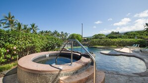 A hot tub with a stone exterior, surrounded by lush greenery and a pool area with lounge chairs. - Aloha Condos, Beach Villas at Kahaluu, Villa 1-202, Beach View, AC (Kailua Kona)