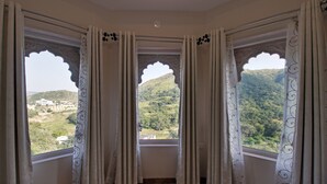 A room with a view of a green landscape through a window with ornate curtains. - Kumbhalgarh Fort Resort (Kumbhalgarh)