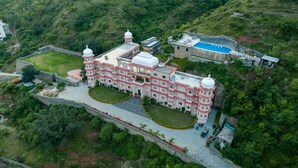 A large, multi-story building with a central courtyard, surrounded by lush greenery and a swimming pool. - Kumbhalgarh Fort Resort (Kumbhalgarh)