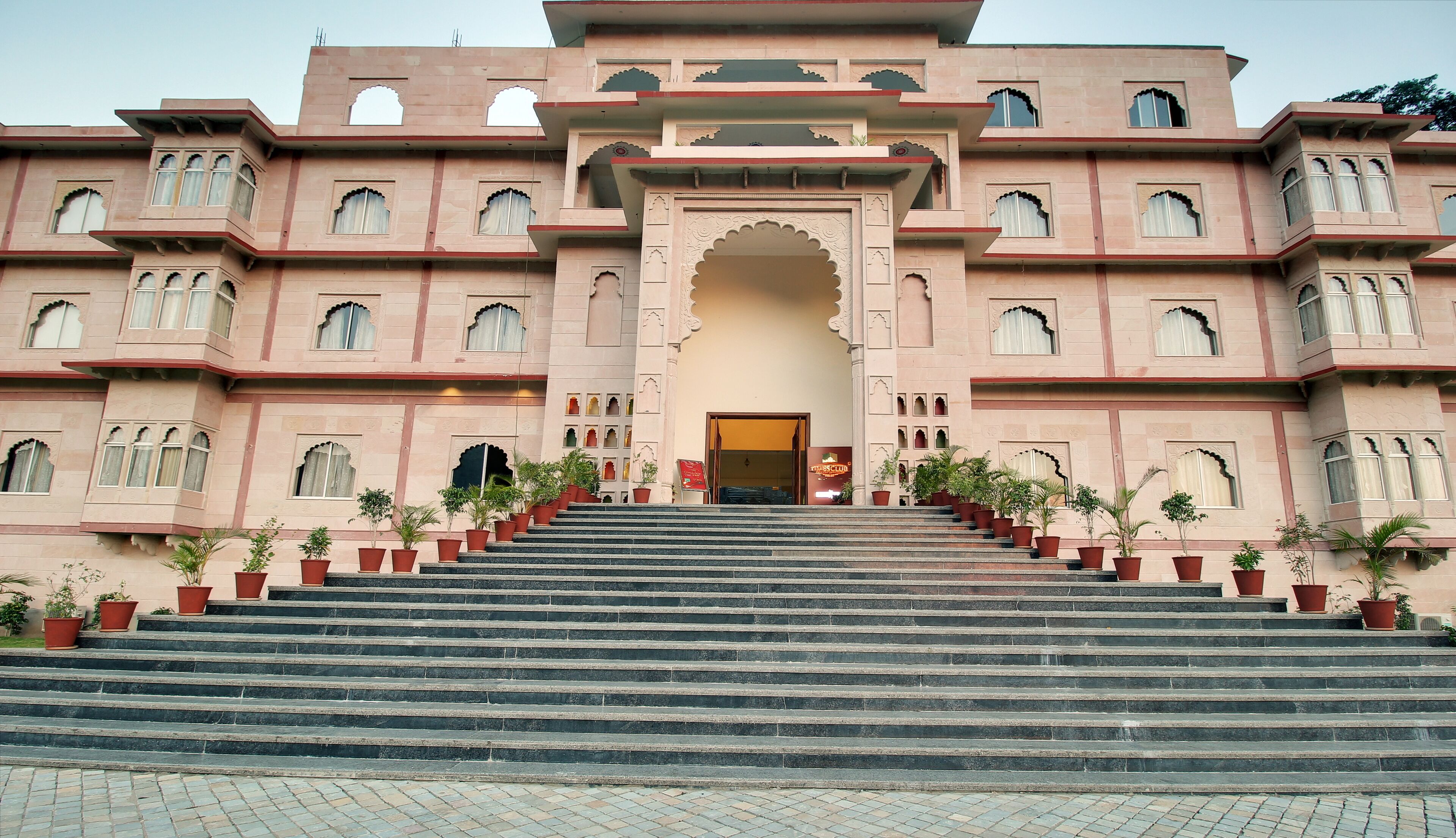 A grand building with multiple balconies and arched windows, featuring a central entrance with steps leading up to it.