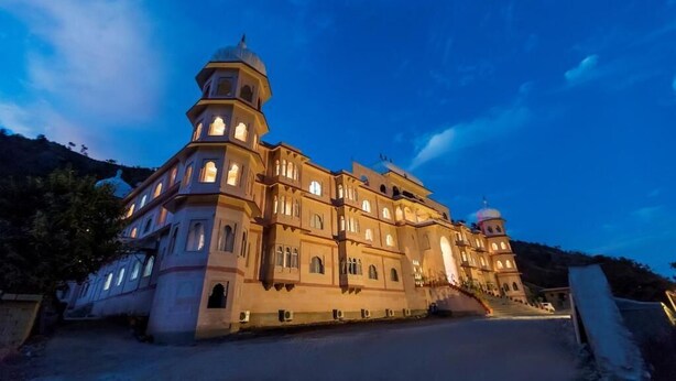 A large, multi-story building with a central dome and multiple smaller domes, surrounded by a mountainous landscape. - Kumbhalgarh Fort Resort (Kumbhalgarh)