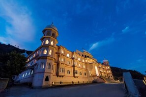 A large, multi-story building with a central dome and multiple smaller domes, surrounded by a mountainous landscape. - Kumbhalgarh Fort Resort (Kumbhalgarh)