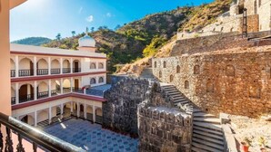 A courtyard with a stone wall, a white building with arches, and a dome. - Kumbhalgarh Fort Resort (Kumbhalgarh)