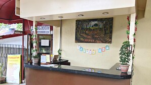 A hotel reception desk with a painting of a forest path, a sign for the "Famous Inn" with listed amenities, and a "Waiting Room" sign. - Famous Inn (Tagaytay)