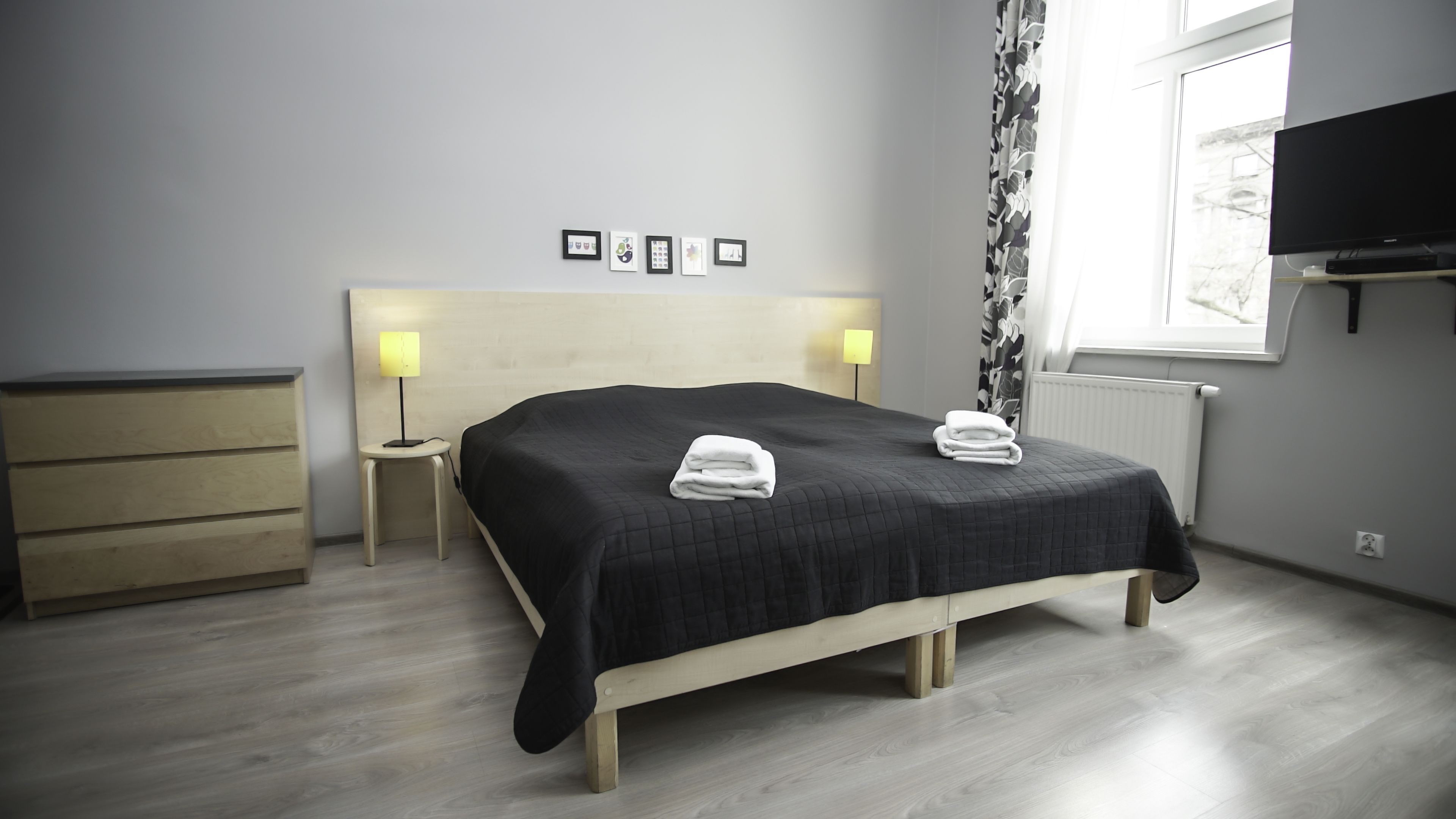 Una habitación de hotel moderna con una cama, lámparas de noche, un aparador y un televisor.