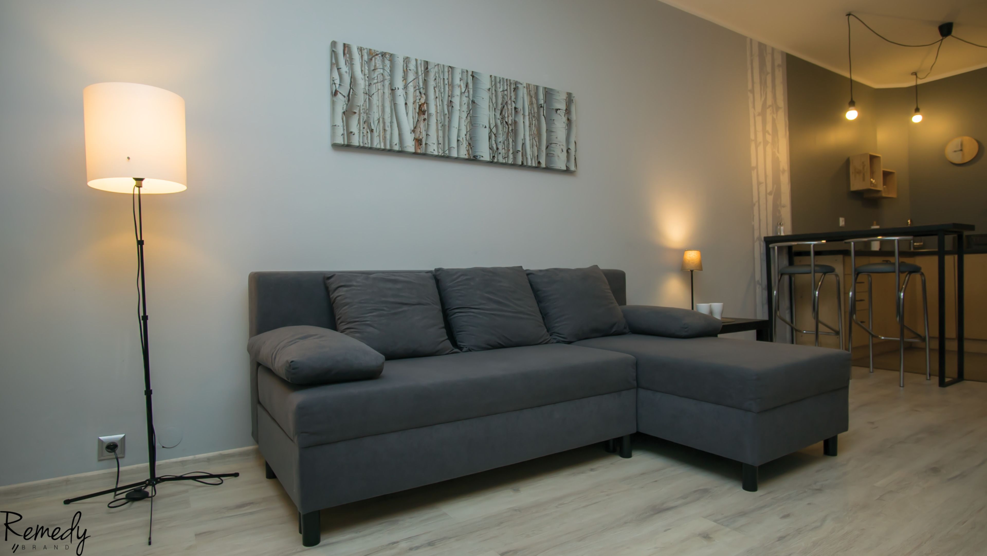 A modern living room with a grey sectional sofa, a floor lamp, and a painting on the wall.
