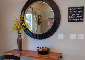 A mirror with a black frame, a vase with yellow flowers, and a bowl of dried plants on a wooden table.
