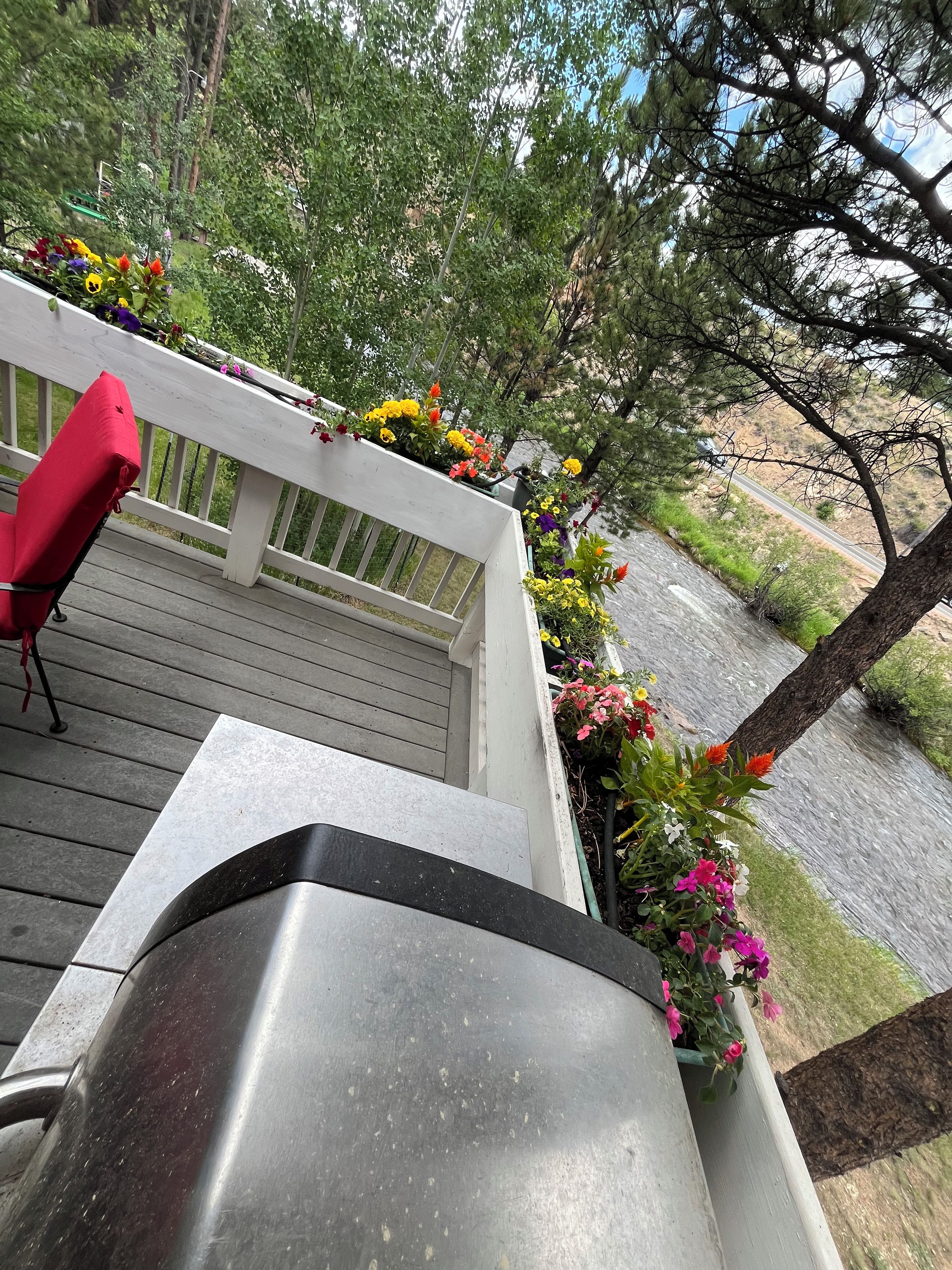 A deck with a red chair, a metal grill, and flower planters with various flowers.