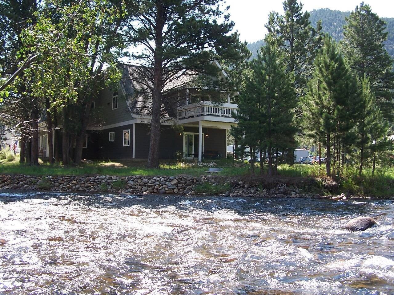 Une maison avec un mur de soutènement en pierre et une rivière devant.