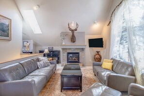 A modern living room with leather sofas, a fireplace, and a mounted deer head.