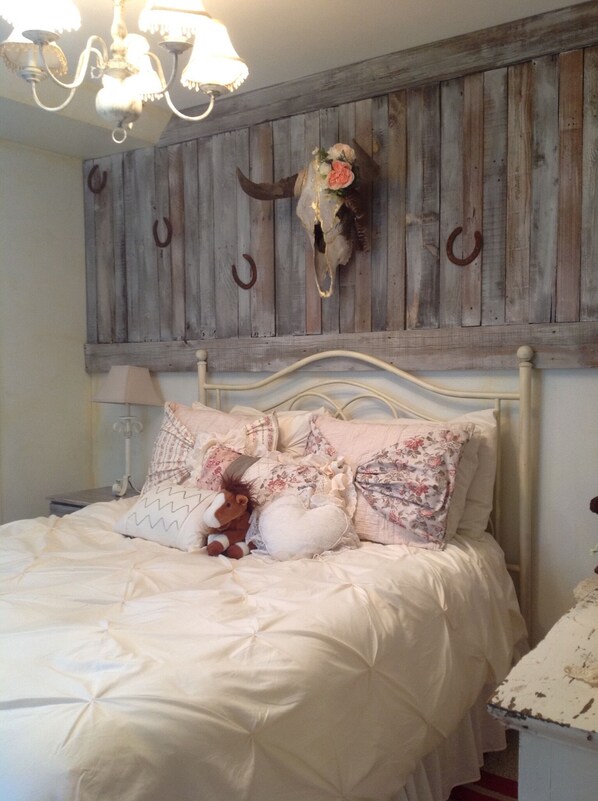 A bedroom with a bed, pillows, a stuffed toy, a wooden headboard, and a chandelier.