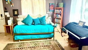 Un dormitorio con cama, estantería, escritorio y ventana con cortinas.