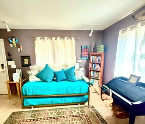 Un dormitorio con cama, estantería, escritorio y ventana con cortinas.